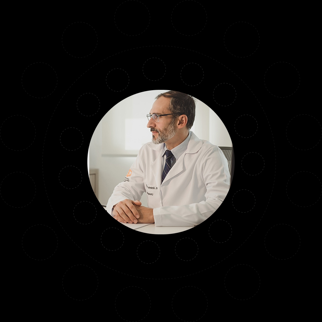 Dr. Antônio Brunetto Neto de jaleco sentado em seu consultório